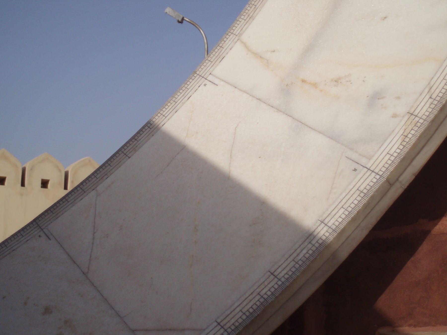 An enormous stone equatorial sundial at Jantar Mantar in Jaipur, with a triangular gnomon ramp and a curved quadrant marked with hour lines.