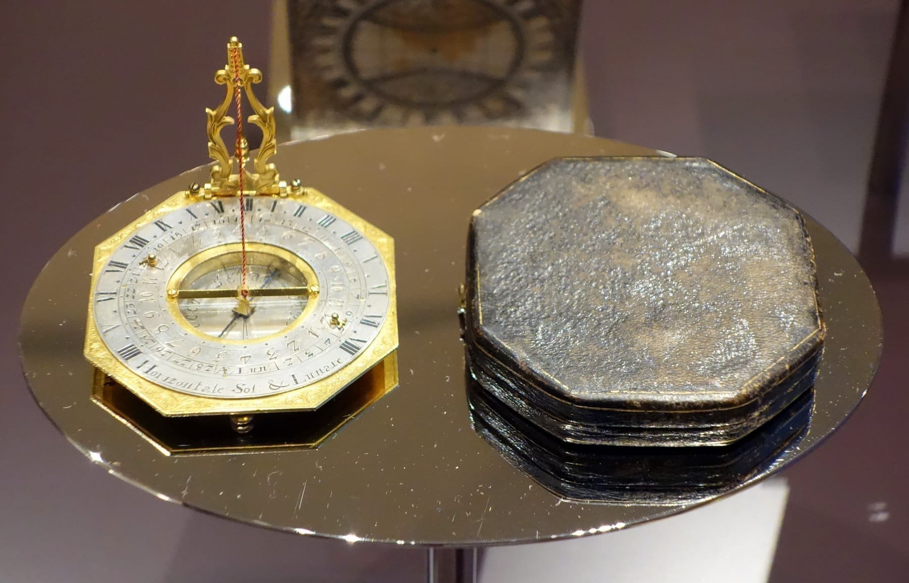 A brass portable horizontal sundial in a wooden case, with the triangular gnomon raised and the hour face visible.