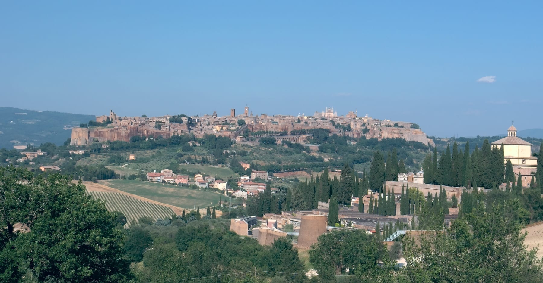 A panoramic view of Orvieto, Italy, showing the medieval town built on tall vertical tuff cliffs rising from the surrounding plain.