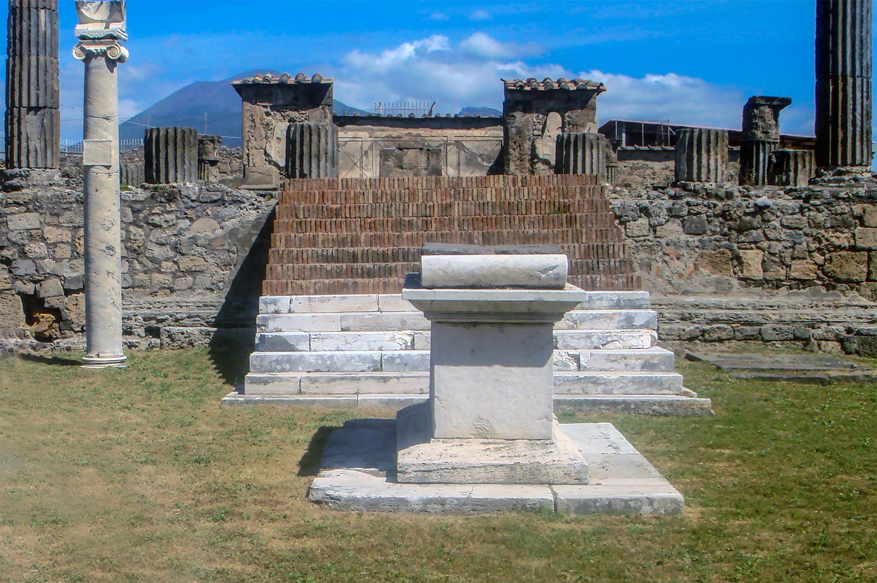 The columns and podium of the Temple of Apollo in Pompeii, with the ancient Roman sundial visible on its stepped base.