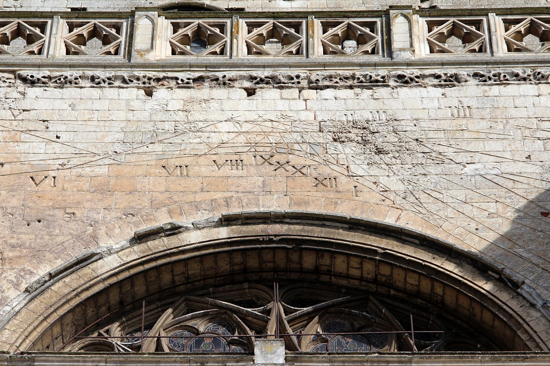 A stone-coloured vertical sundial on a brick cathedral wall, with clearly engraved hour lines radiating from a central gnomon.