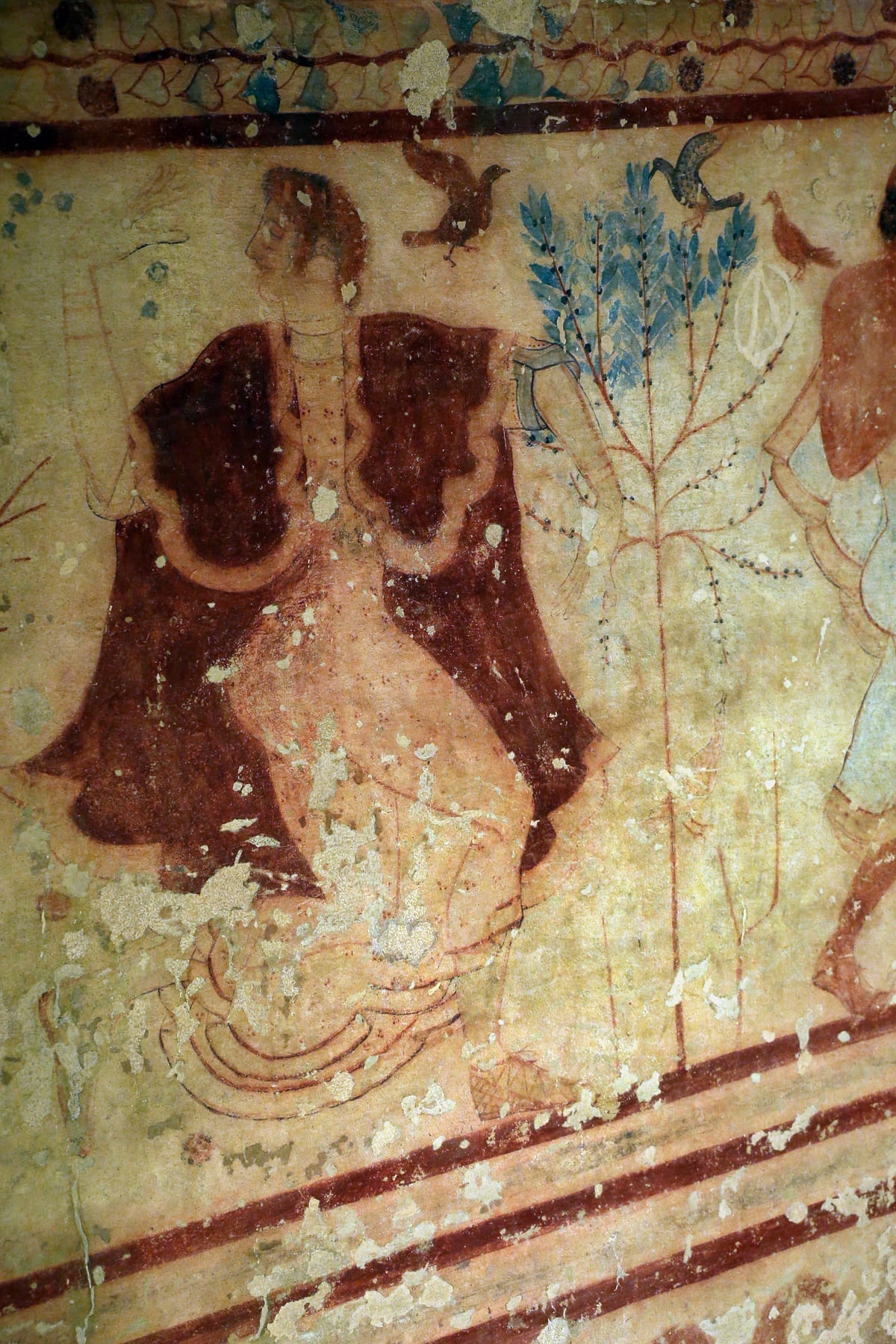 An Etruscan fresco showing a female dancer in a long patterned robe, painted in warm earth tones on a tomb wall.