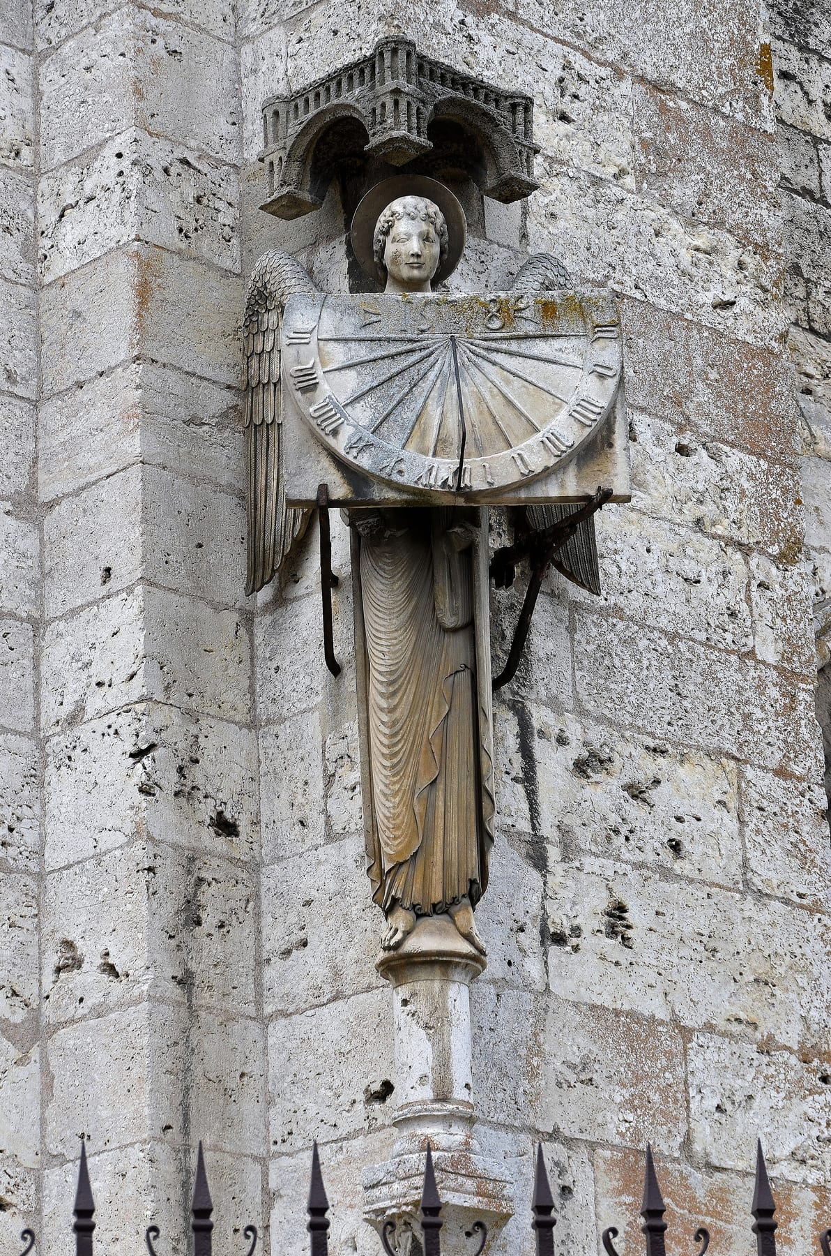 A stone angel on the south facade of Chartres Cathedral holding a sundial, with the 1528 date visible on the dial face.